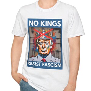 May include: White t-shirt featuring a graphic with the text "NO KINGS" above a portrait of a man wearing a crown, with the words "RESIST FASCISM" below. The graphic has red, blue, and orange accents.