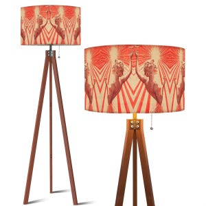 May include: Two wooden tripod lamps with patterned shades. The shades feature a repeating design of a woman with outstretched arms against a red and cream background. The lamps have a warm, inviting aesthetic, suitable for home decor.