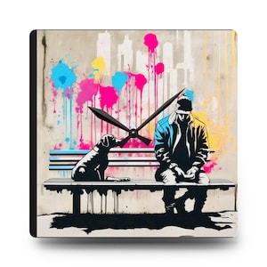 May include: Square wall clock featuring a graffiti-style illustration of a person and a dog on a bench. The background has colorful paint splatters and a city skyline. The clock hands are black.