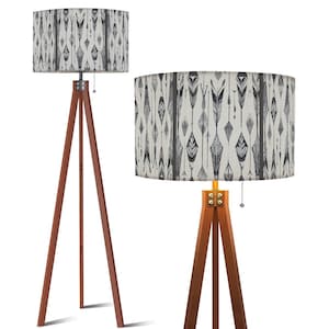 May include: Two wooden tripod floor lamps. The lampshades are rectangular and feature a repeating pattern of black and gray arrows and geometric shapes on a white background. The wooden legs are a dark brown color.