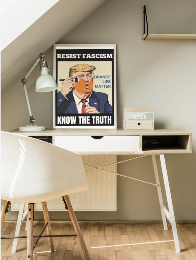 May include: A framed poster with the text "RESIST FASCISM" and "KNOW THE TRUTH" features a caricature of a man with orange skin and blonde hair. The poster also includes the text "ORANGE LIES MATTER". A white desk, chair, and lamp are also visible.