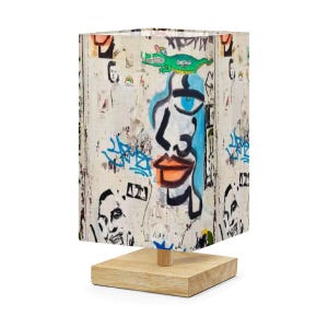 May include: A rectangular lamp with a wooden base and a shade featuring graffiti art. The shade displays a blue and black face design, a green alligator, and various other graffiti elements. The lamp is a unique piece of home decor.