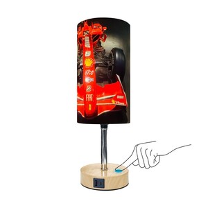 May include: A cylindrical table lamp featuring a red Formula 1 race car design. The lamp has a chrome stem and a wooden base with a USB port. The lamp is being turned on with a finger.