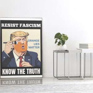 May include: A framed poster with the text "RESIST FASCISM" and "KNOW THE TRUTH". The image features a caricature of a man applying orange makeup, with the words "ORANGE LIES MATTER". The poster is displayed indoors.