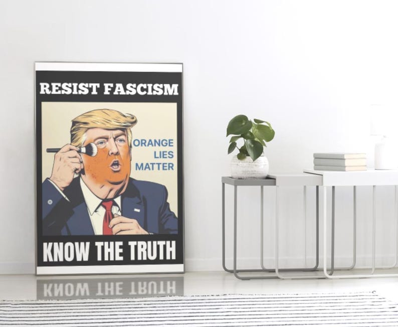 May include: A framed poster with the text "RESIST FASCISM" and "KNOW THE TRUTH". The image features a caricature of a man applying orange makeup, with the words "ORANGE LIES MATTER". The poster is displayed indoors.