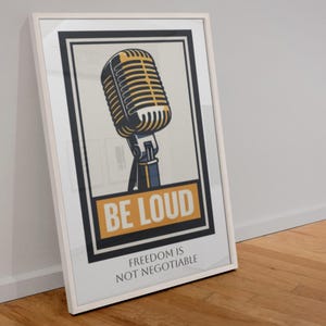 May include: Framed poster with a retro microphone illustration in yellow and black on a cream backdrop. The words "BE LOUD" are in a yellow box, with "FREEDOM IS NOT NEGOTIABLE" below. The frame is white.