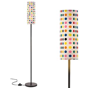 May include: A tall floor lamp with a cylindrical lampshade. The lampshade is white with a pattern of colorful polka dots in various sizes. The lamp has a dark metal pole and a round base. The lamp is plugged into an electrical outlet.