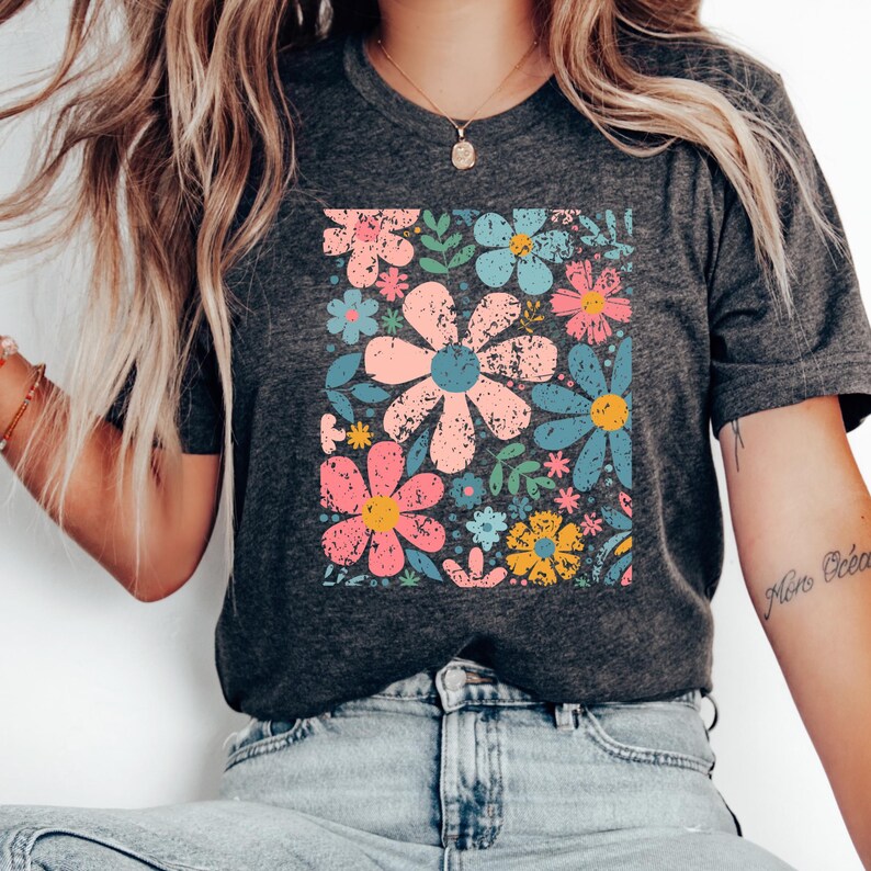 以下が含まれることがあります： 鮮やかな花柄が特徴の濃いグレーのTシャツ。デザインには、ヴィンテージ風の大きなピンク、青、黄色の花が含まれています。緑の葉と小さな花がパターンを完成させています。
