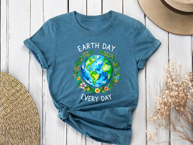 Puede incluir: Una camiseta azul turquesa con un gr&aacute;fico blanco de la Tierra rodeada de flores y el texto "Earth Day Every Day".