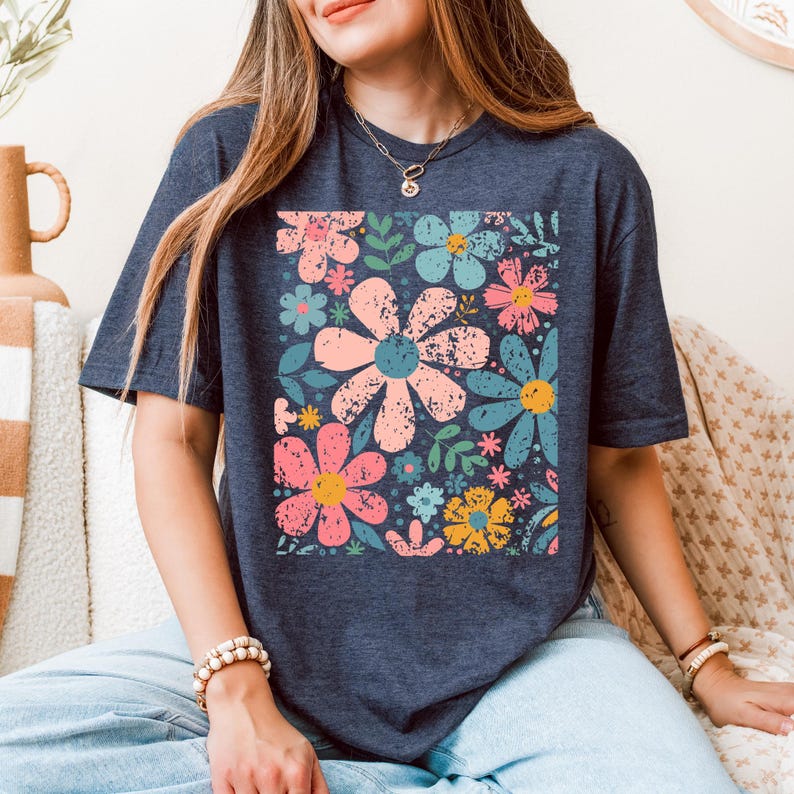 以下が含まれることがあります： ピンク、青、黄色の大柄な花柄が特徴のネイビーブルーのTシャツ。 花は使い古したようなヴィンテージ感があります。 ゆったりとしたフィット感で、半袖です。