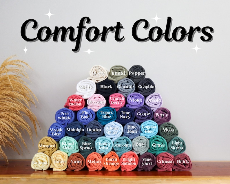 May include: A pyramid of rolled fabric swatches in various colors, labeled with names like "Khaki", "Pepper", "Black", "Granite", "Graphite", "Watermelon", "Blossom", "Berry", "Peri Winkle", "Flo Blue", "Topaz Blue", "True Navy", "Grape", "Berry", "Jean", "Mystic Blue", "Midnight", "Denim", "Blue Spruce", "Chalk Mint", "Seafoam", "Bay", "Grass", "Light Green", "Yam", "Melon", "Burnt Orange", "Bright Salmon", "Vine Yard", "Crimson", and "Brick". The text "Comfort Colors" is at the top of the image.