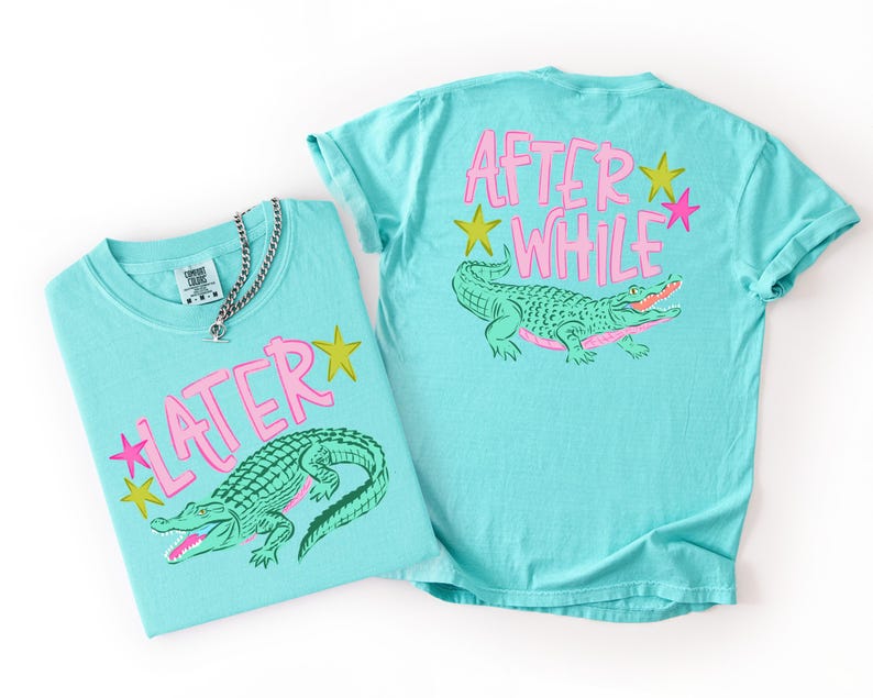 May include: Two turquoise t-shirts with a graphic of a green alligator and the text "LATER" and "AFTER WHILE" in pink. The shirts also feature pink and yellow star graphics. A silver chain necklace is on one shirt.