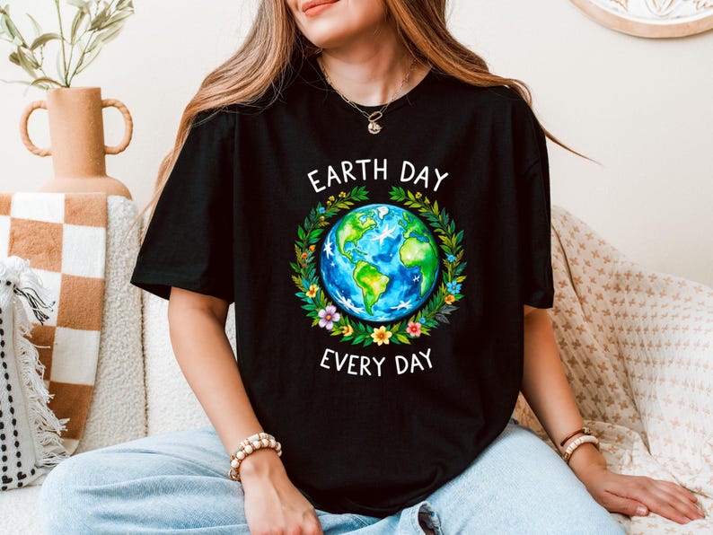 Puede incluir: Una camiseta negra con un gr&aacute;fico de una Tierra colorida rodeada de flores y hojas. El texto "Earth Day Every Day" est&aacute; impreso en blanco debajo del gr&aacute;fico.