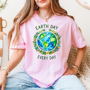 Puede incluir: Una camiseta rosa con una corona verde alrededor de un globo terr&aacute;queo azul y verde. El texto "Earth Day Every Day" est&aacute; impreso en la camiseta.
