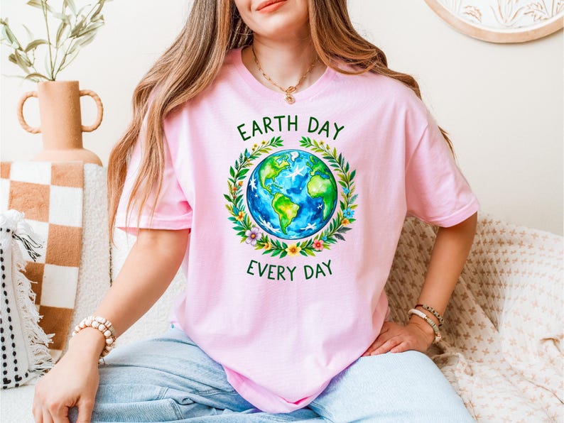 Puede incluir: Una camiseta rosa con una corona verde alrededor de un globo terr&aacute;queo azul y verde. El texto "Earth Day Every Day" est&aacute; impreso en la camiseta.