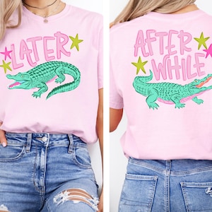 May include: Pink t-shirt featuring a green alligator graphic with the text "LATER" on the front and "AFTER WHILE" on the back. The design includes pink text and star accents.