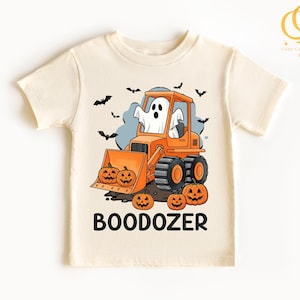 Peut inclure: T-shirt cr&egrave;me avec un motif d'Halloween. Le design comprend un bulldozer orange avec un fant&ocirc;me conducteur, des citrouilles et des chauves-souris. Le mot "BOODOZER" est imprim&eacute; en lettres noires en dessous.