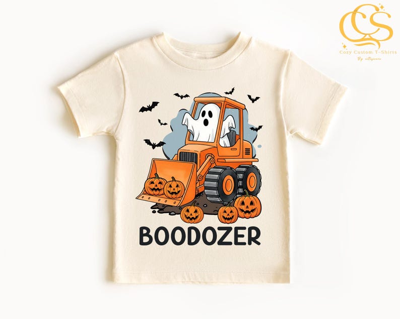 Peut inclure: T-shirt cr&egrave;me avec un motif d'Halloween. Le design comprend un bulldozer orange avec un fant&ocirc;me conducteur, des citrouilles et des chauves-souris. Le mot "BOODOZER" est imprim&eacute; en lettres noires en dessous.