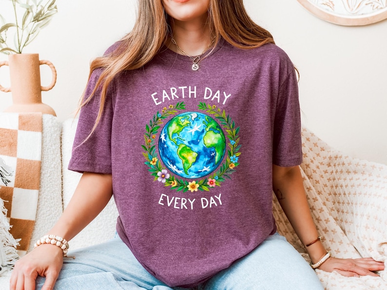 Puede incluir: Una camiseta morada con un gr&aacute;fico de la Tierra rodeada de flores y el texto "Earth Day Every Day".