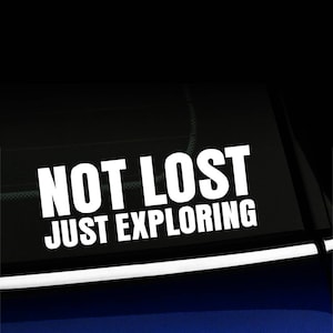 Puede incluir: Calcomanía de vinilo blanco con el texto "Not Lost Just Exploring" sobre un fondo negro. La calcomanía está en la ventana trasera de un coche.
