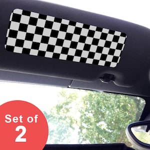 May include: A rectangular car sun visor cover featuring a black and white checkered pattern. The accessory is designed to fit over a vehicle sun visor. A red circular graphic in the corner displays the white text Set of 2, indicating the quantity.