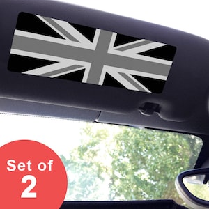 May include: A set of two black and white Union Jack car sun visor covers. The covers feature a grey and white Union Jack design on a black background. The text "Set of 2" is visible in the image.