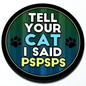 Puede incluir: Una pegatina redonda con borde negro y fondo rayado verde y azul. La pegatina dice "Tell your cat I said pspspps" en texto blanco con un "cat" azul y un "pspspps" verde. Hay dos huellas de patas negras a cada lado del texto.