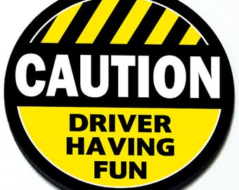 May include: A yellow and black round sticker with diagonal black stripes and the text "CAUTION DRIVER HAVING FUN".