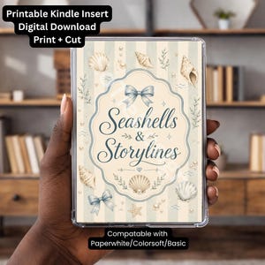 May include: A rectangular Kindle insert featuring a cream and light blue striped background with illustrations of seashells, pearls, and blue bows. The center displays a decorative frame with the text Seashells & Storylines in dark blue script.