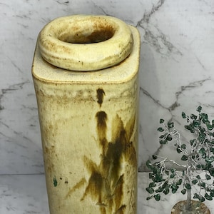May include: A beige ceramic jar with a lid. The jar has a rectangular base and a cylindrical body with a bamboo design in brown. The lid is circular with a raised edge. The jar is likely used for storage or decoration.