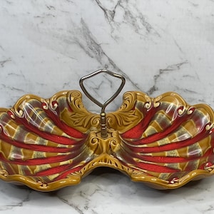 May include: A vintage two-section serving dish with a handle. The dish is shell-shaped with a brown and red color scheme. The handle is silver-colored. The dish has a decorative, ornate design.