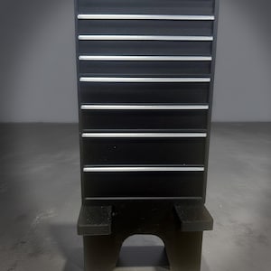 May include: A black tool organizer with multiple horizontal shelves and the word "Tools" printed at the top. The organizer has a sturdy base and is designed to hold various tools. The shelves are accented with silver trim.