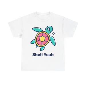 Puede incluir: Camiseta blanca con un diseño de tortuga de dibujos animados. La tortuga tiene un cuerpo turquesa, un caparazón amarillo y rosa, y el texto "Shell Yeah" en azul marino. La tortuga tiene una cara sonriente y un pequeño gráfico de estrella.