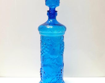 May include: A cobalt blue glass decanter with a grape design. The decanter has a round body and a tall, slender neck.
