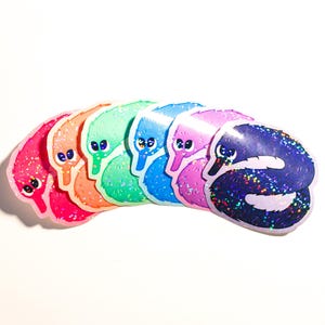 May include: A set of eight worm-shaped stickers with glitter accents. The stickers are arranged in a rainbow pattern, with each worm a different color: pink, orange, green, blue, purple, light blue, pink, and black.