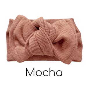 Pode incluir: Uma faixa de cabe&ccedil;a de malha canelada cor mocha com um grande la&ccedil;o. A palavra "Mocha" est&aacute; impressa em escrita preta abaixo da faixa de cabe&ccedil;a. A faixa de cabe&ccedil;a &eacute; feita de um material macio e el&aacute;stico.