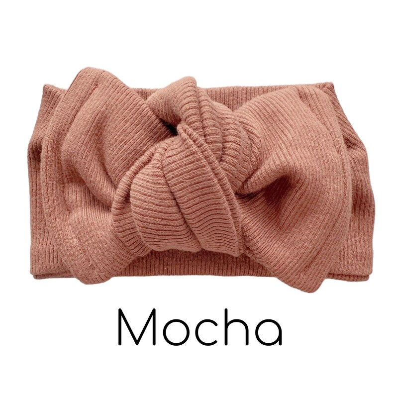 Pode incluir: Uma faixa de cabe&ccedil;a de malha canelada cor mocha com um grande la&ccedil;o. A palavra "Mocha" est&aacute; impressa em escrita preta abaixo da faixa de cabe&ccedil;a. A faixa de cabe&ccedil;a &eacute; feita de um material macio e el&aacute;stico.