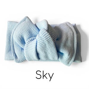 Pode incluir: Uma faixa de cabe&ccedil;a azul claro em malha canelada com um design de n&oacute;. A palavra "Sky" est&aacute; impressa em preto na parte inferior da imagem. A faixa de cabe&ccedil;a &eacute; feita de um material macio e texturizado.