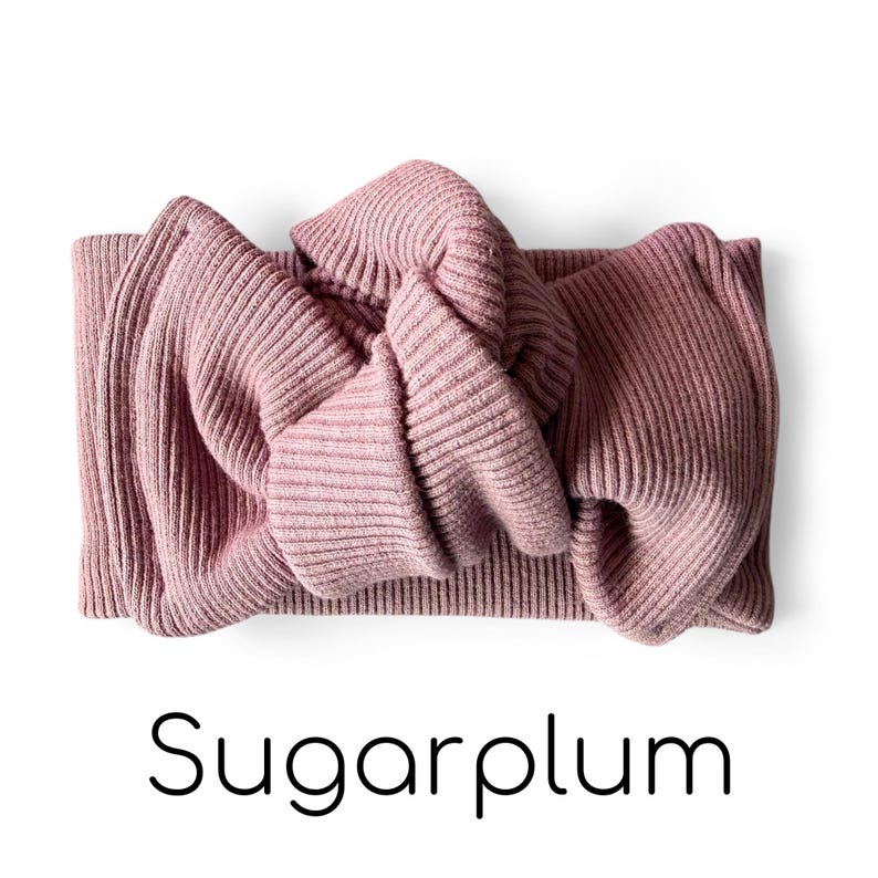 Pode incluir: Faixa de cabelo de malha canelada cor malva com detalhe de la&ccedil;o atado. A palavra "Sugarplum" est&aacute; escrita em preto, com uma fonte moderna, abaixo da faixa. A faixa &eacute; feita de um material macio e texturizado.