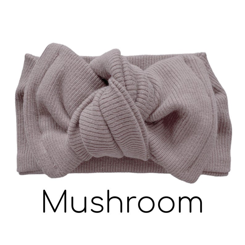 Pode incluir: Faixa de cabelo canelada na cor cogumelo com um la&ccedil;o atado no centro. A palavra "Mushroom" est&aacute; impressa em preto abaixo. Um acess&oacute;rio de cabelo elegante.