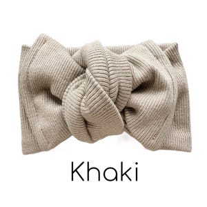 Pode incluir: Uma faixa de cabe&ccedil;a de malha canelada cor c&aacute;qui com um design de la&ccedil;o atado. A palavra "Khaki" est&aacute; impressa em preto na parte inferior da imagem. A faixa de cabe&ccedil;a &eacute; feita de um material macio e el&aacute;stico.