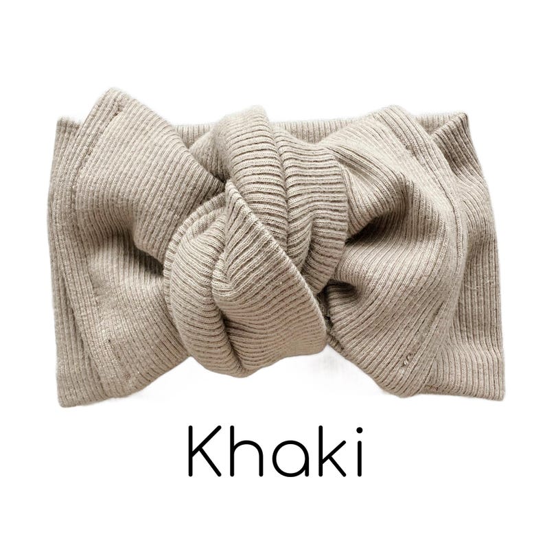 Pode incluir: Uma faixa de cabe&ccedil;a de malha canelada cor c&aacute;qui com um design de la&ccedil;o atado. A palavra "Khaki" est&aacute; impressa em preto na parte inferior da imagem. A faixa de cabe&ccedil;a &eacute; feita de um material macio e el&aacute;stico.