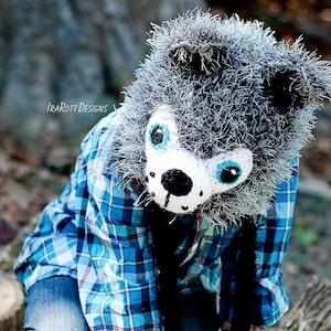 May include: A child wearing a blue and white plaid shirt and blue jeans is wearing a gray and white crocheted wolf mask with blue eyes. The mask has a black nose and mouth.