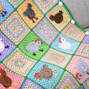 Pode incluir: Um cobertor de beb&eacute; de crochet colorido com um design de patchwork que apresenta v&aacute;rios quadrados coloridos com galinhas de crochet em diferentes cores.