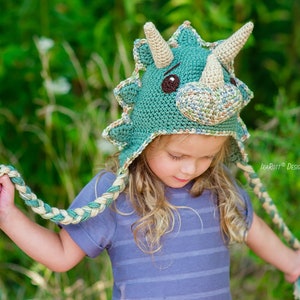 Puede incluir: Un gorro de triceratops de ganchillo hecho a mano en tonos verde azulado, beige y marr&oacute;n. El gorro presenta tres cuernos beige, ojos marrones y una cinta trenzada. El gorro est&aacute; dise&ntilde;ado con un tema de dinosaurios y es adecuado para ni&ntilde;os.