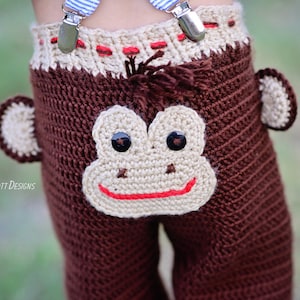 Puede incluir: Pantalones de bebé de crochet marrón con una cara de mono en la parte posterior. La cara del mono tiene una nariz marrón, una boca roja y ojos negros.