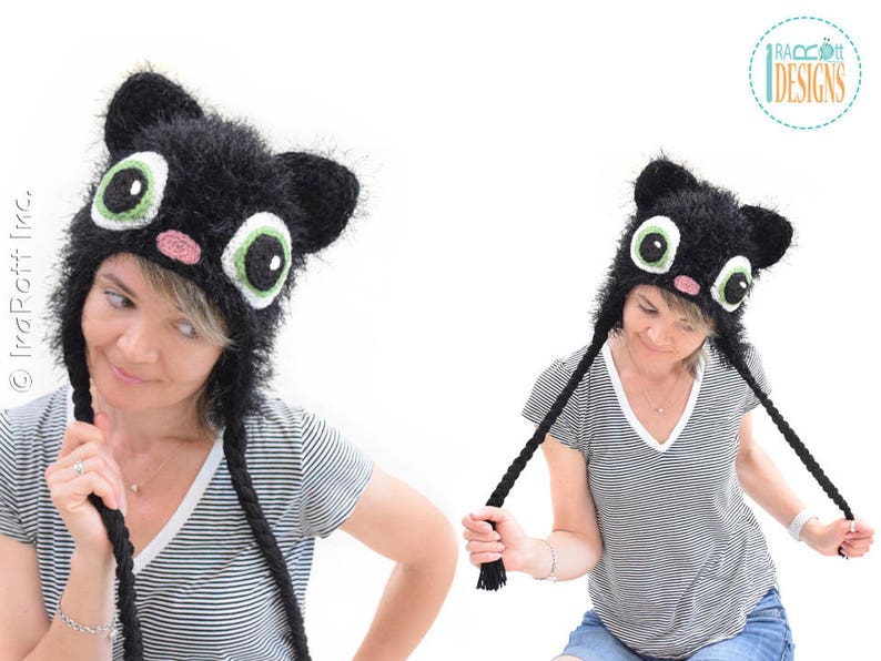 May include: A black cat hat with large, cartoonish eyes, ears, and a pink nose. The hat has long, braided ties. The hat is worn by a person wearing a striped shirt.