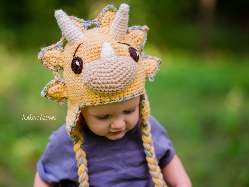 Puede incluir: Un gorro de Triceratops tejido a mano en tonos amarillos, beige y marr&oacute;n. El gorro presenta una cara de dinosaurio con cuernos, ojos y hocico. Trenzas de hilo cuelgan a los lados. Dise&ntilde;ado para un ni&ntilde;o.