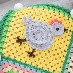 Pode incluir: Um cobertor de croch&ecirc; com um design de patchwork colorido. O cobertor apresenta uma aplica&ccedil;&atilde;o de pintinho de croch&ecirc; cinza com bico e pernas marrons. O cobertor &eacute; enfeitado com uma borda de croch&ecirc; verde.
