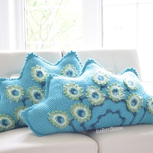 May include: Two turquoise crochet pillows with a floral design. The pillows are star-shaped with a scalloped edge. The floral design features green and blue accents, adding a decorative touch to the pillows.